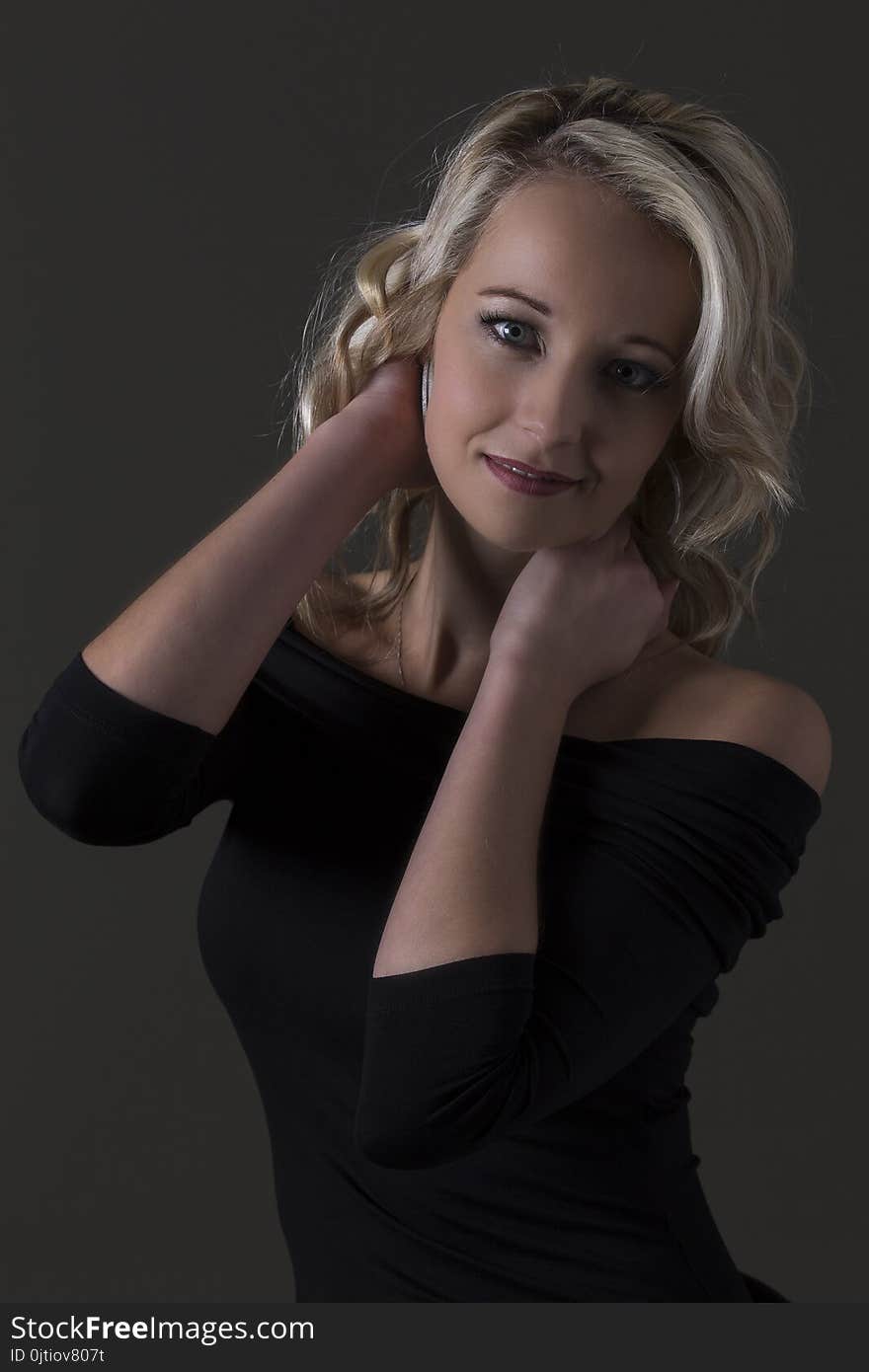 Beautiful blond woman in black top in dark with selective lighting and hands in hair