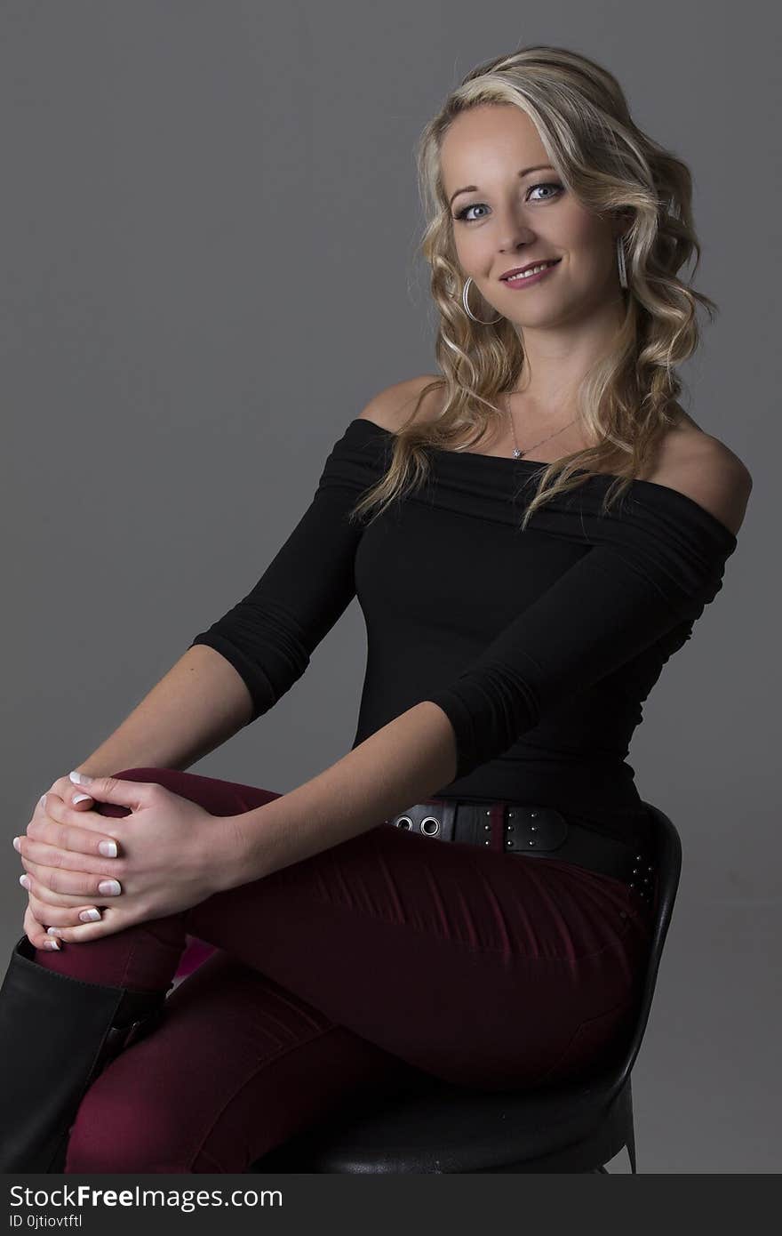 Beautiful blond woman in curly hair and black top and red pants on a grey background