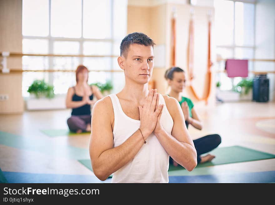 Group of young sporty people practicing yoga lesson with instructor, sitting in Padmasana exercise, Lotus pose with folded hands i