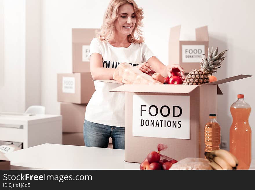 Collect everything. Busy female keeping smile on her face and bowing head while controlling process of food donations. Collect everything. Busy female keeping smile on her face and bowing head while controlling process of food donations