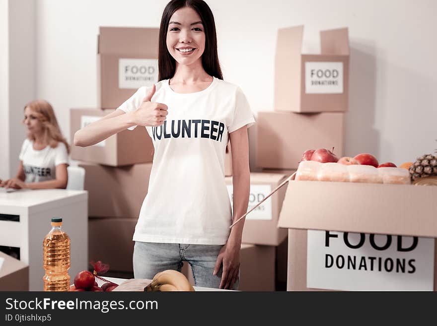 I like it. Attractive international girl being volunteer, keeping smile on face and standing on the foreground near big box. I like it. Attractive international girl being volunteer, keeping smile on face and standing on the foreground near big box