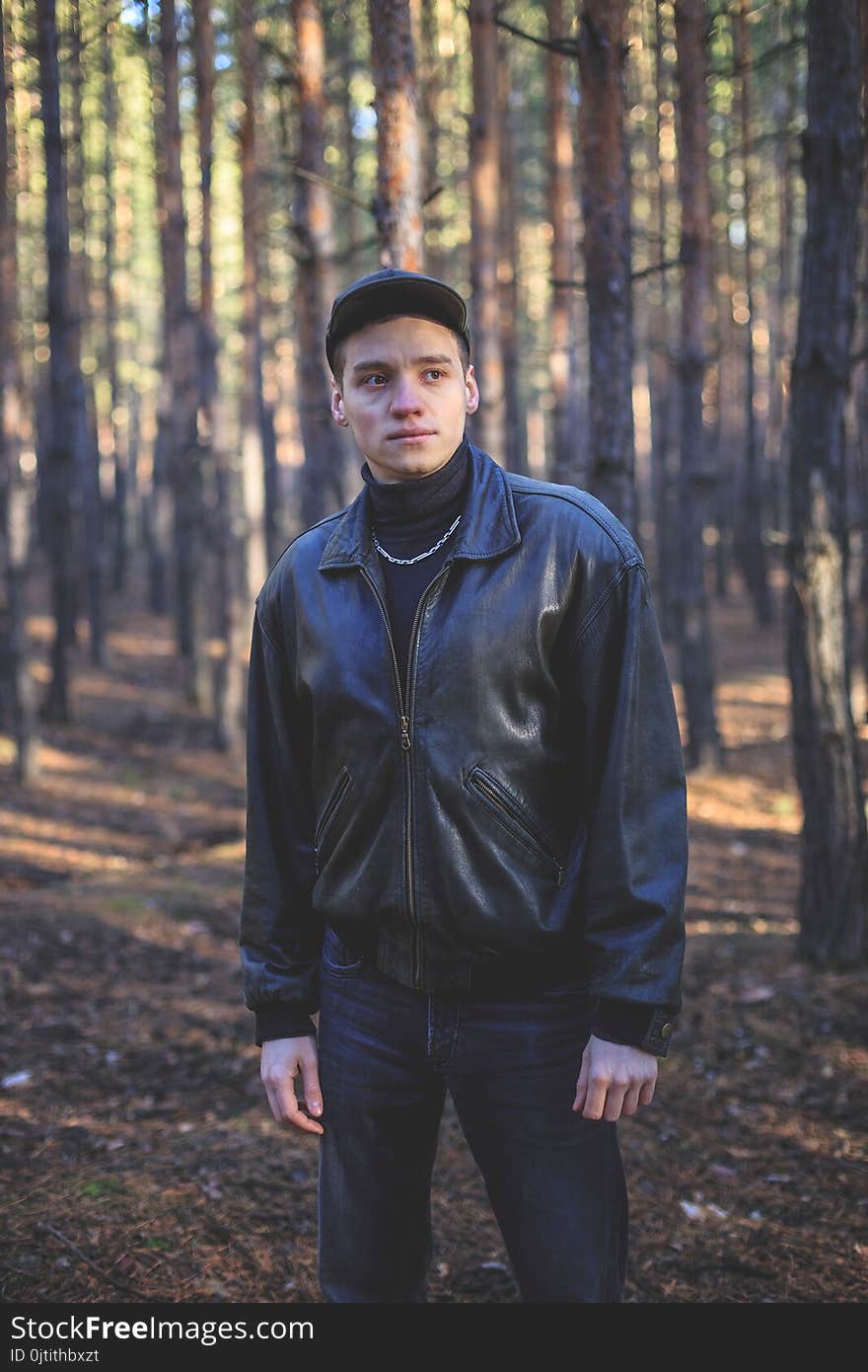 A young man of criminal appearance in a black leather jacket posing in an autumn forest