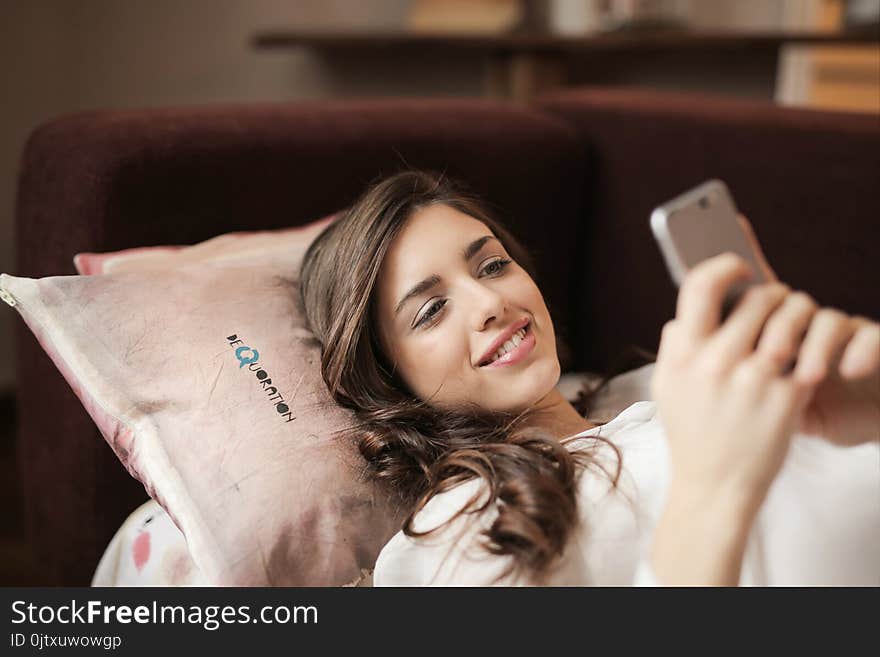 Woman in White Top Holding Smartphone Lying on Couch