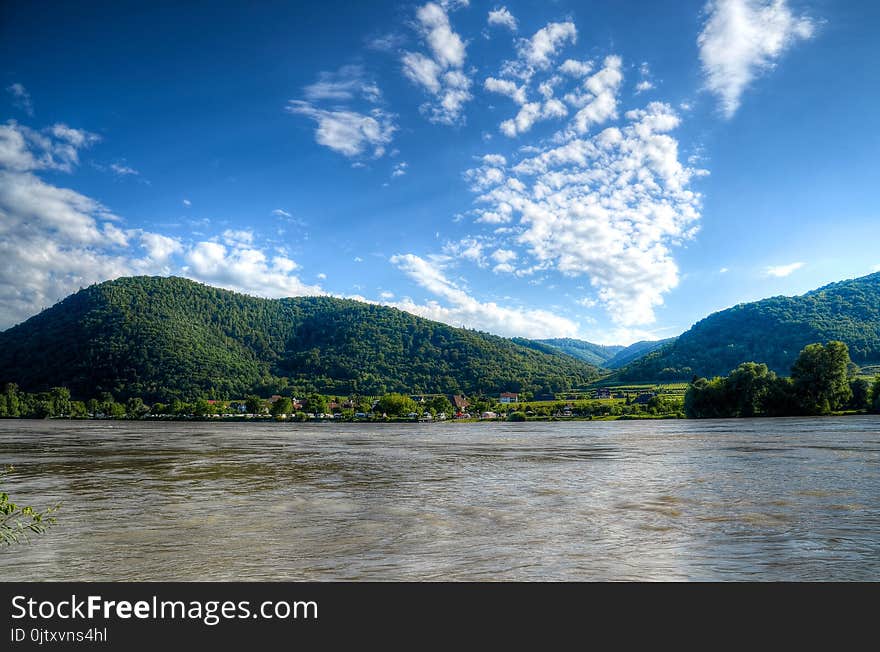 Body of Water Near Mountains Under Blue Sky