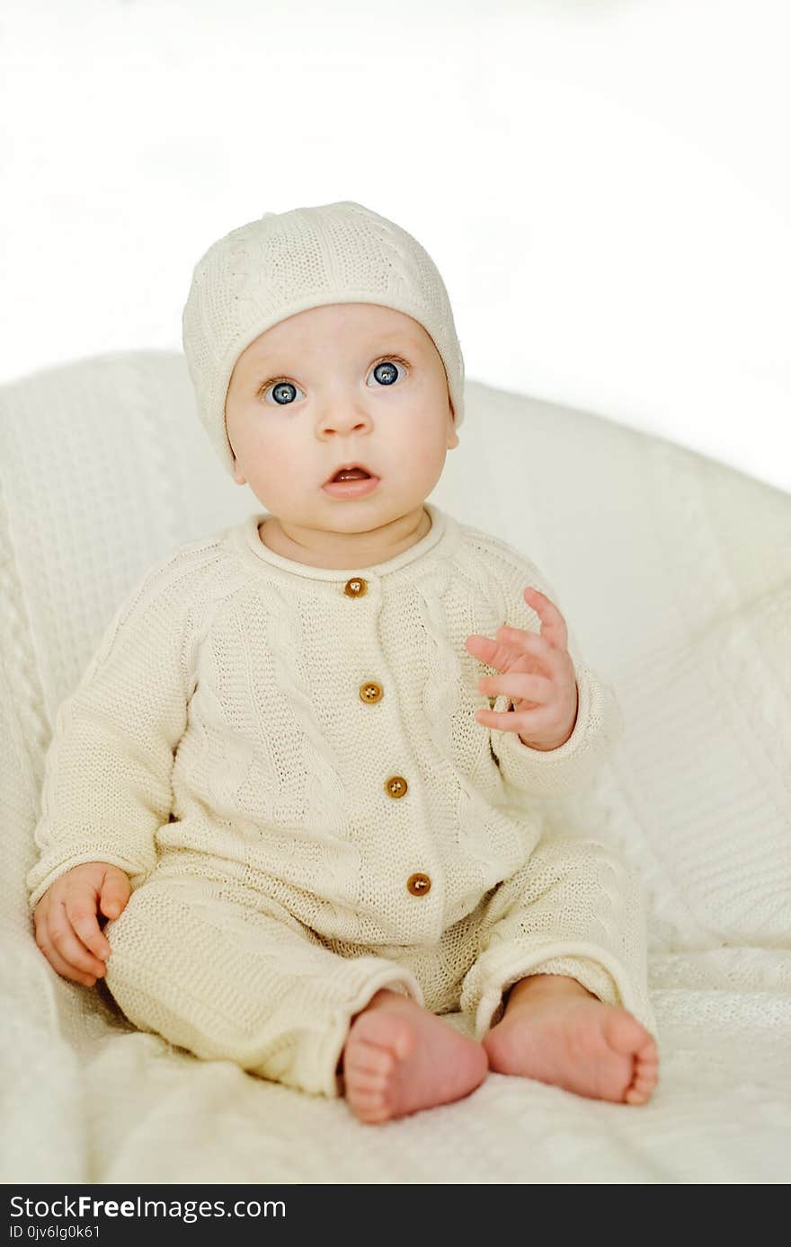 Sweet baby wearing knitted suit is sitting on the chair