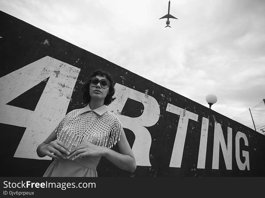 Grayscale Photo of Woman Standing Beside Wall