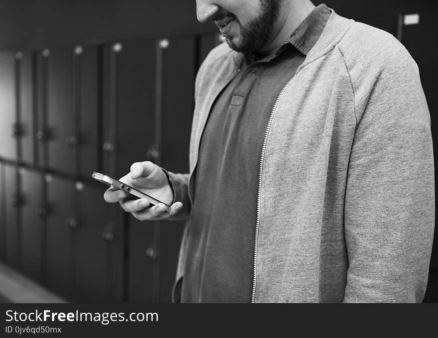 Grayscale Photo of Man Wearing Zip-up Jacket Holding Android Smartphone