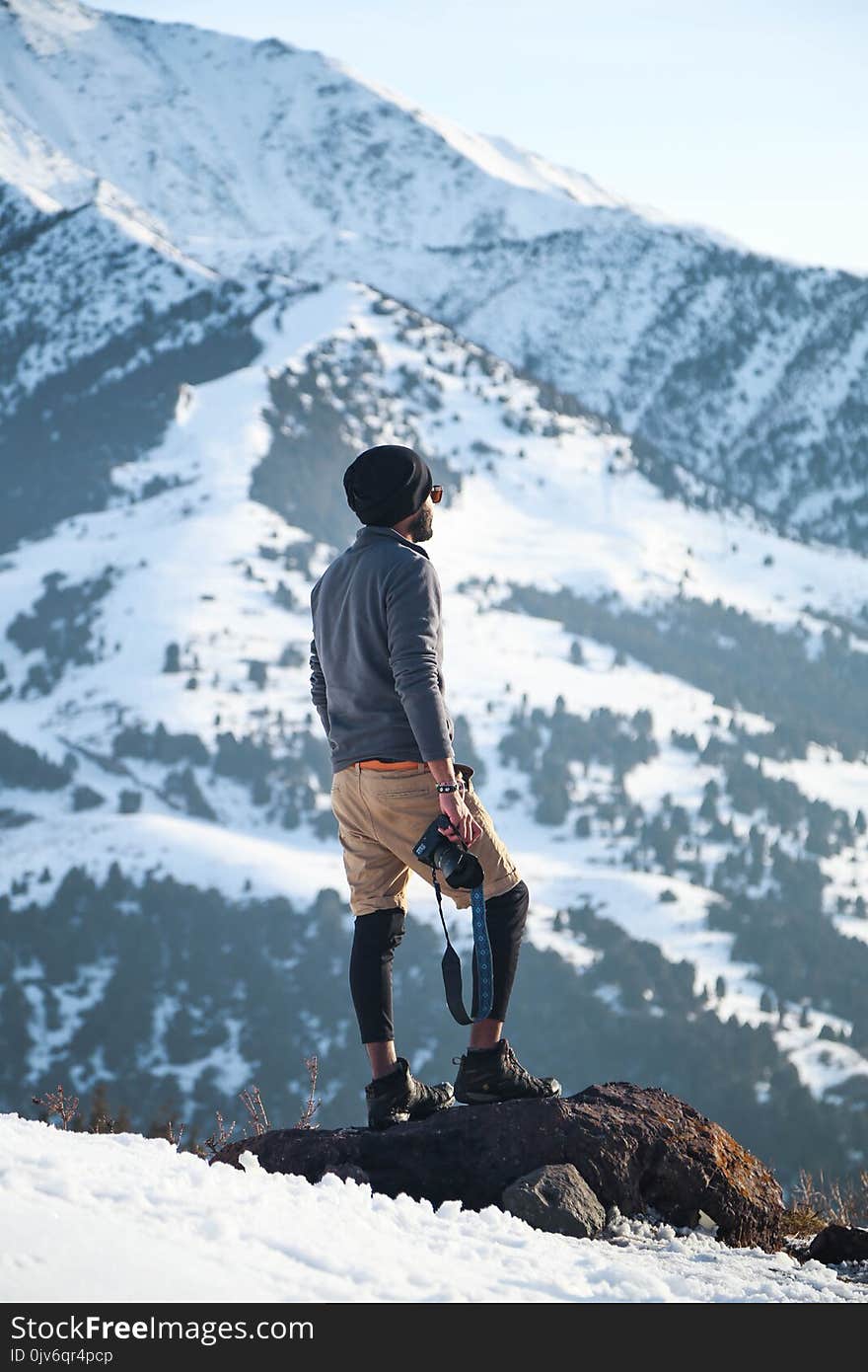 Man Wearing Gray Long-sleeved Shirt and Brown Shorts Holding Black Dslr Camera on Mountain