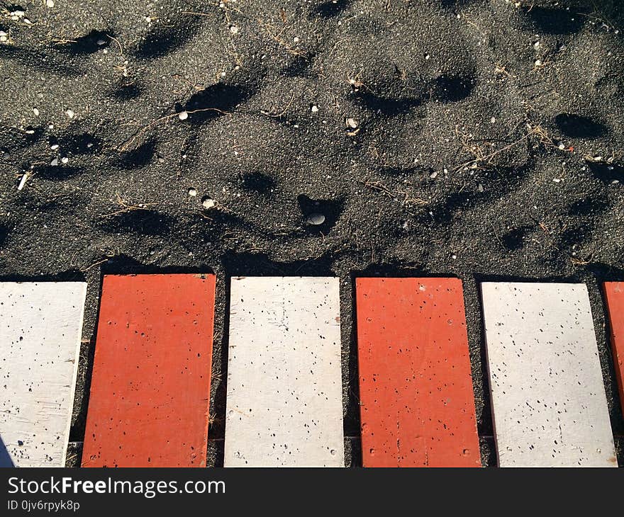 Red and White Metal Planks on Black Sand