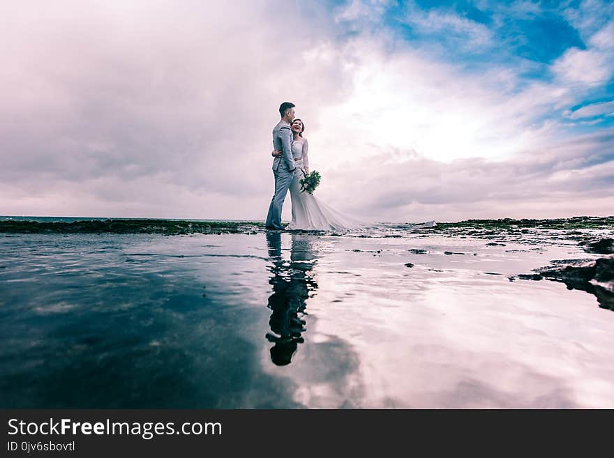 Man in Gray Dress Suit Jacket Embraces Woman Wearing Wedding Gown