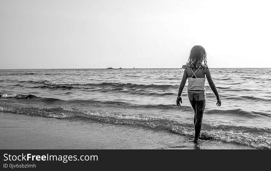 Grayscale Photo of Girl Walking on Seashore With White Spaghetti Strap Top