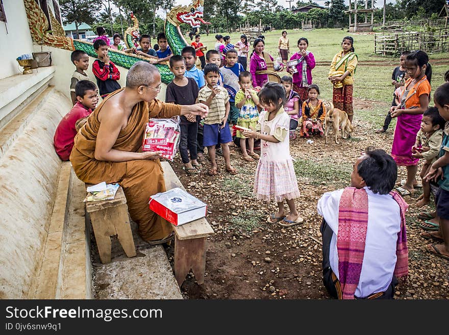 Monk in Front of Children Near Brown Concrete Building