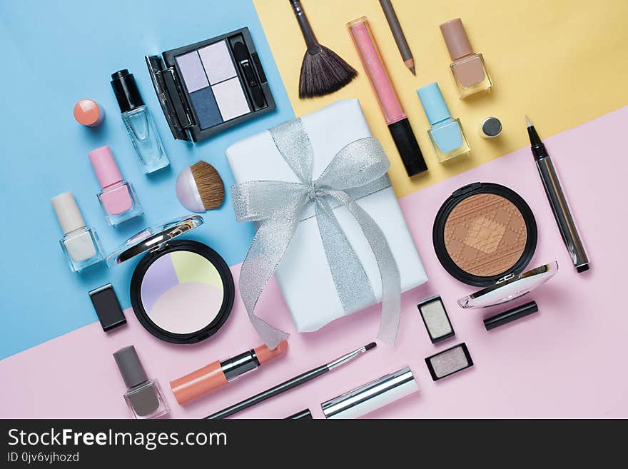 Beauty, decorative cosmetics and gift box with bow. Makeup brushes set and color eyeshadow palette on bright multicolor and blue background , flat lay, top view, Minimalistic style