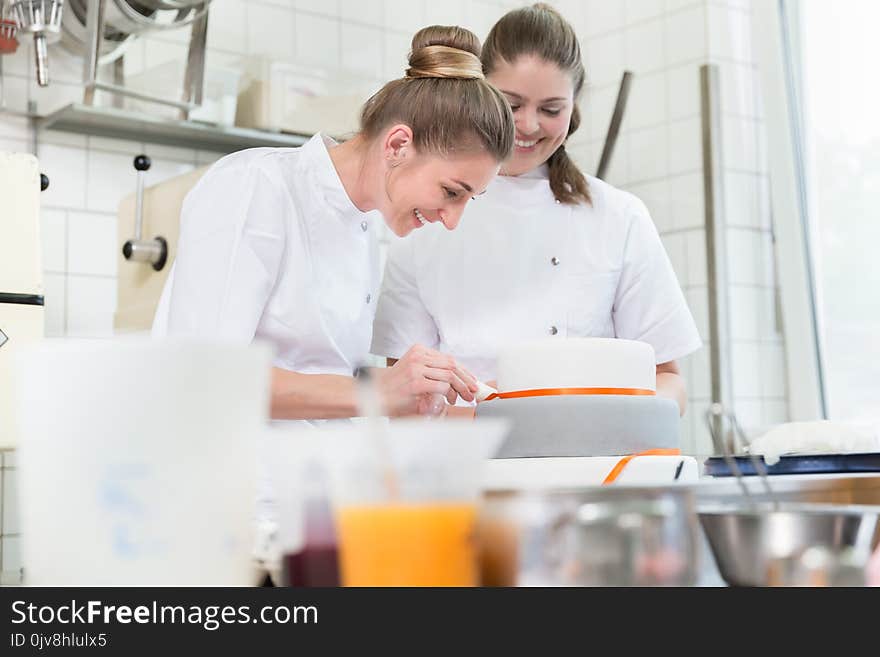 Women in fine bakery or pastry shop baking cakes helping each other. Women in fine bakery or pastry shop baking cakes helping each other