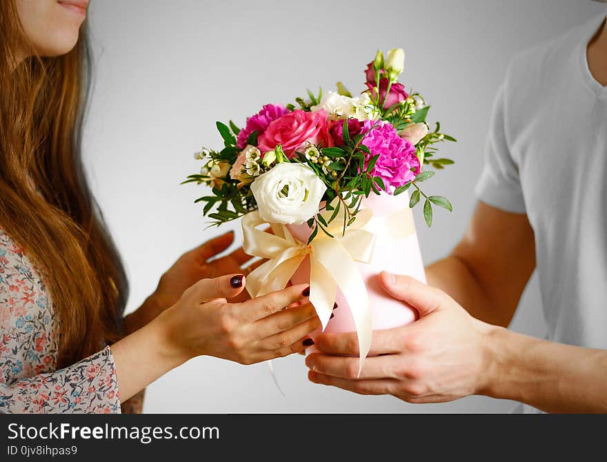 The guy gives a bouquet of flowers to a girl. Composition of flowers in a pink hatbox. Tied with wide white ribbon and bow.