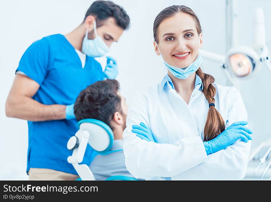 Portrait of a happy and confident female dentist wearing sterile white coat and surgical gloves, while looking at camera in the dental office of a modern clinic with reliable specialists. Portrait of a happy and confident female dentist wearing sterile white coat and surgical gloves, while looking at camera in the dental office of a modern clinic with reliable specialists