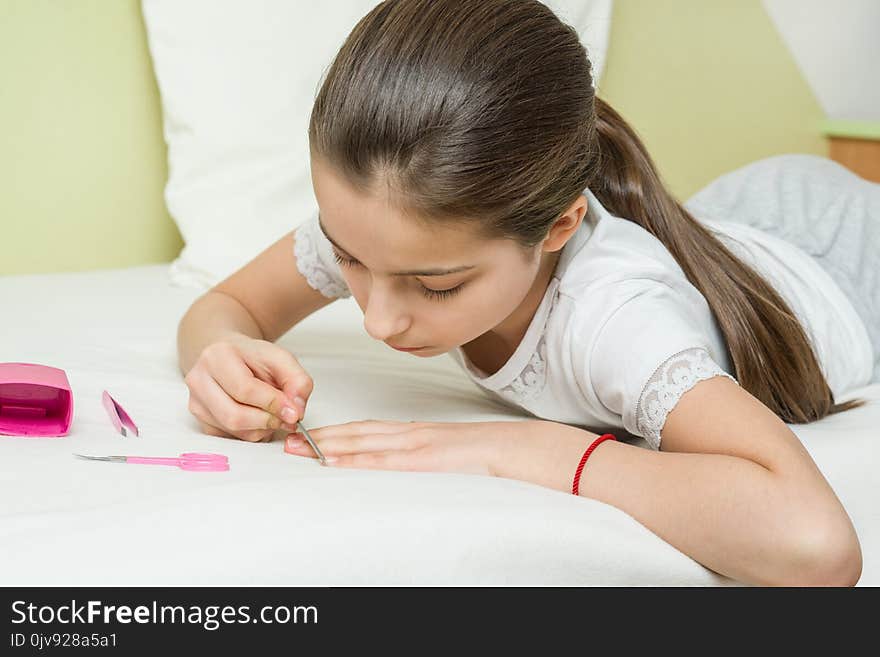 The Girl Is 10 Years Old At Home On The Bed In Her Home Clothes, Nails Her Nails Using Manicure Accessories.