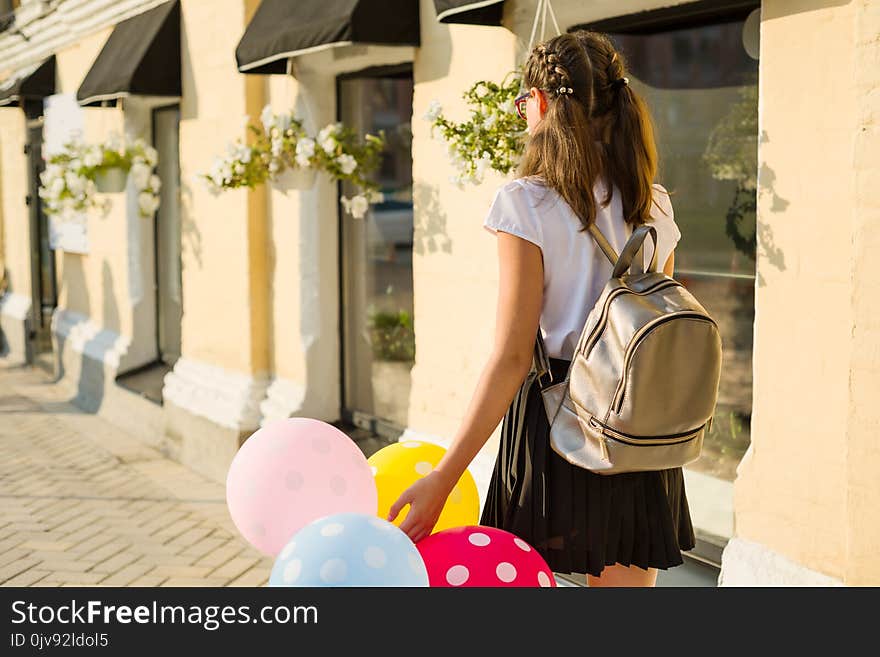 Back view. Girl teenager high school student with balloons, in school uniform goes along the city street