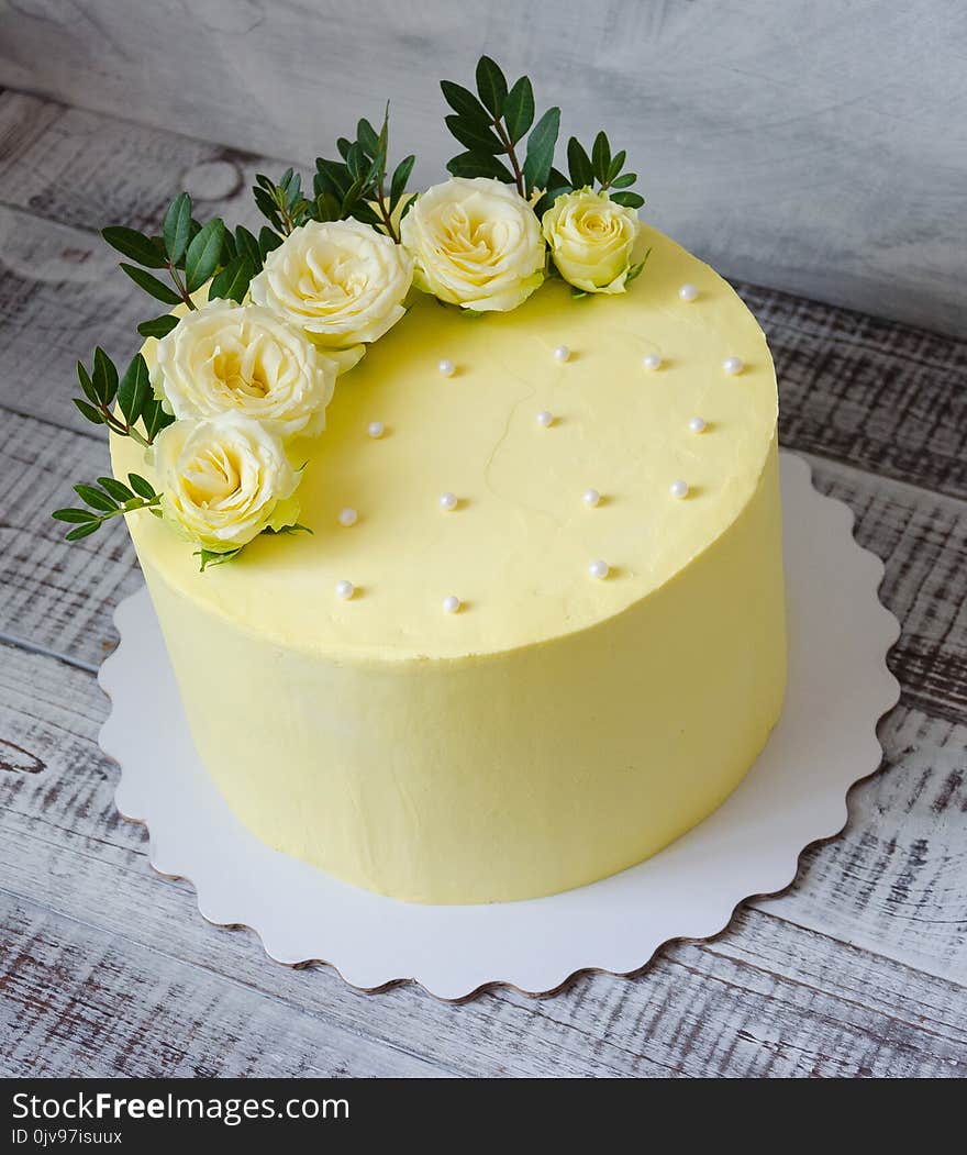 A yellow cream cheese cake with roses and greenery