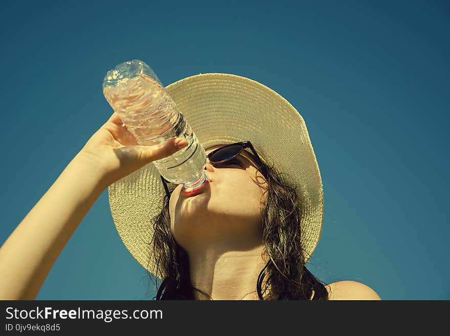 Young Girl Is Drinking Water On The Blue Sky Background.