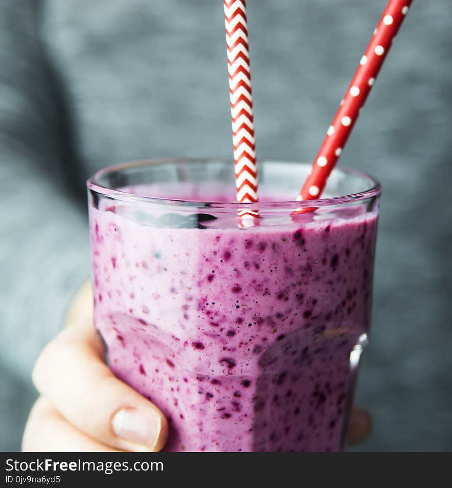 Banana currant smoothies of violet color in a transparent glass in female hands. On a gray background, in dark tones. Close up. Banana currant smoothies of violet color in a transparent glass in female hands. On a gray background, in dark tones. Close up