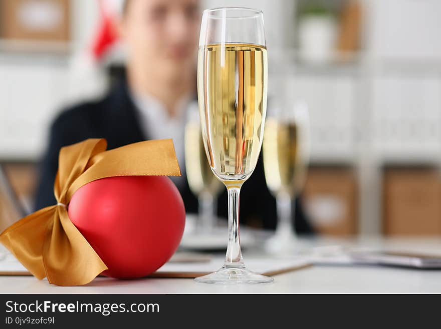 Businessman in santa hat against a background of a glass with champagne and ball decorating a Christmas tree