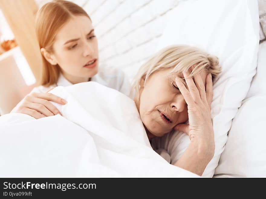 Girl is nursing elderly women in bed at home. Woman is feeling bad, girl is concerned.