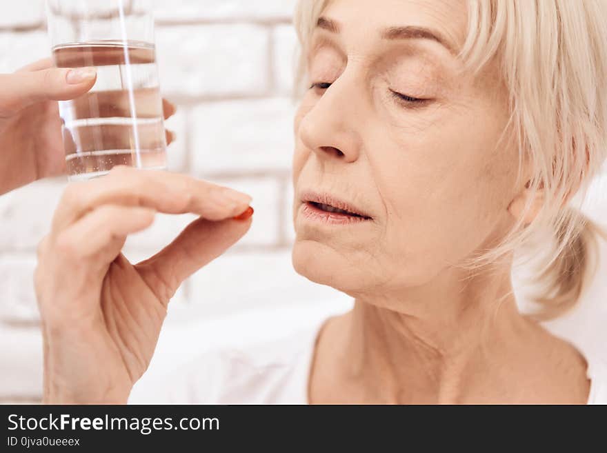 Girl is nursing elderly woman at home. Girl brings water and pills.