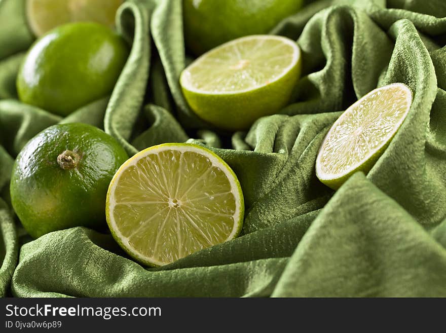 Group of whole and cut fresh limes on a green satin