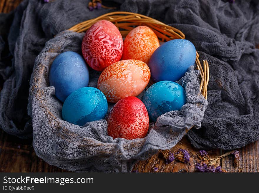 Wicker basket with unusual colored Easter eggs in different colors. Still-life on a wooden background.