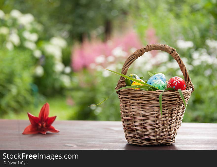 Basket with painted eggs and red lilly flower on table in garden