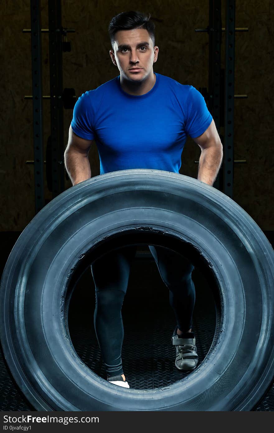 Portrait of a strong athlete with a large heavy wheel in the gym