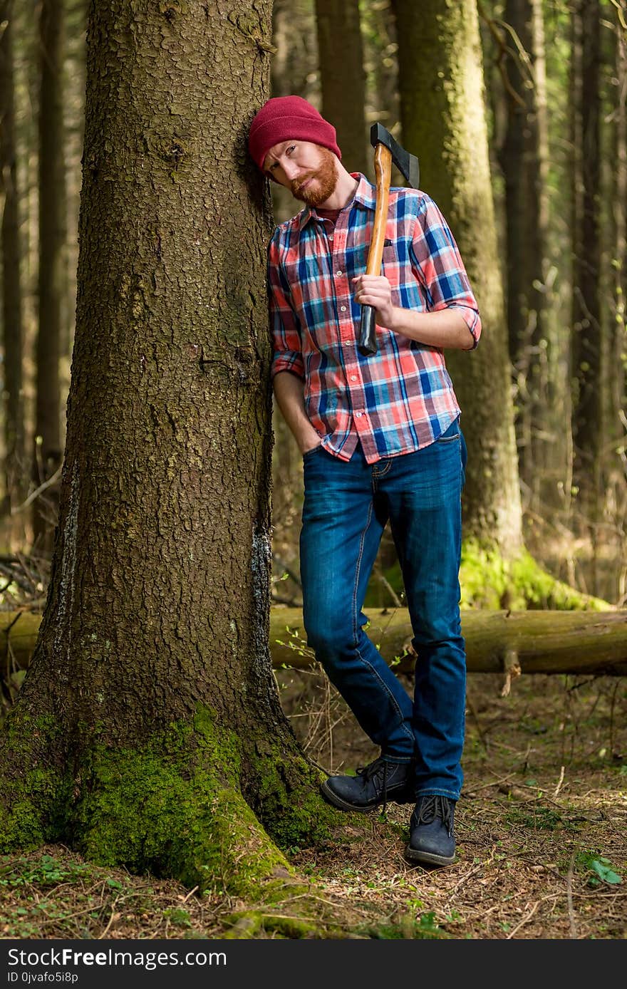 Tired bearded lumberjack with an ax resting, leaning against a t