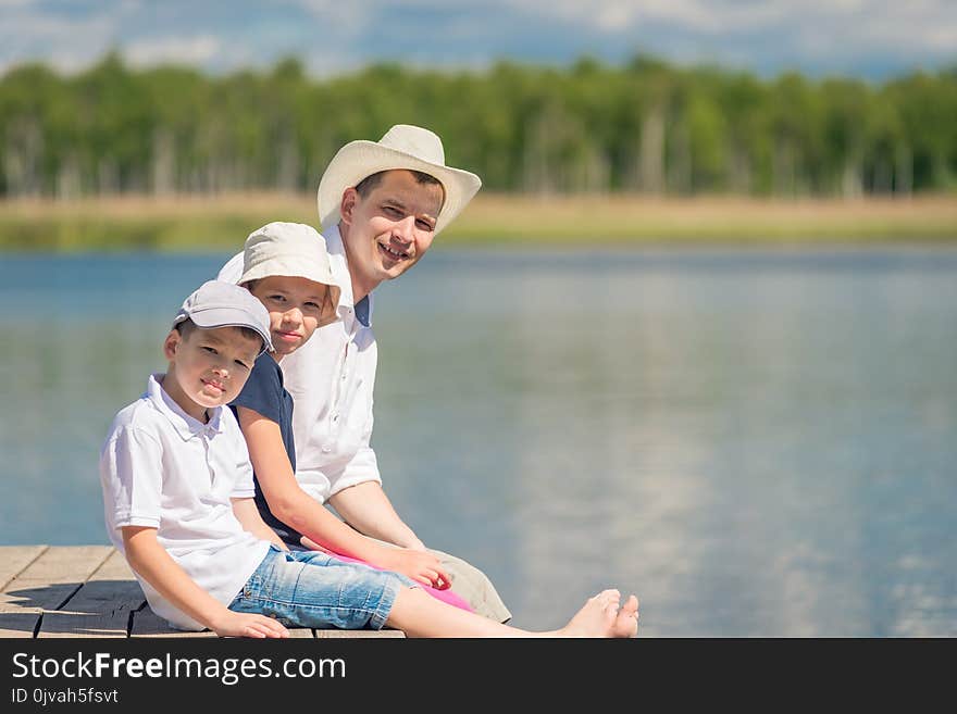 Portrait of father and children sitting on a wooden pier near the lake