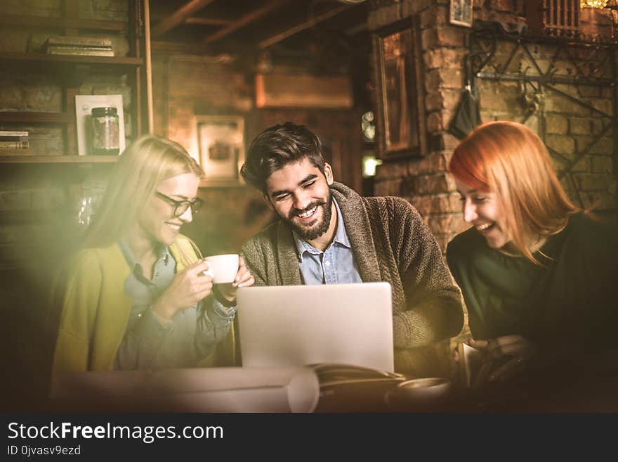 Three young smiling student using laptop together at cafe. Small group people. Three young smiling student using laptop together at cafe. Small group people.