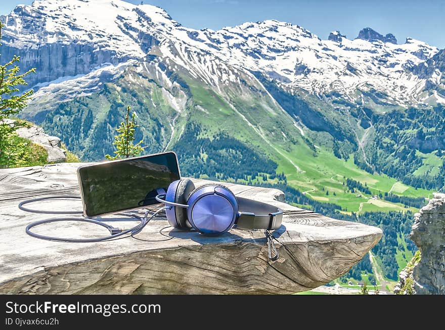 Cell phone with headphones on a wooden table on the background of the Swiss Alps and mountain scenery.