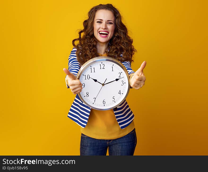 Smiling woman on yellow background with clock showing thumbs up