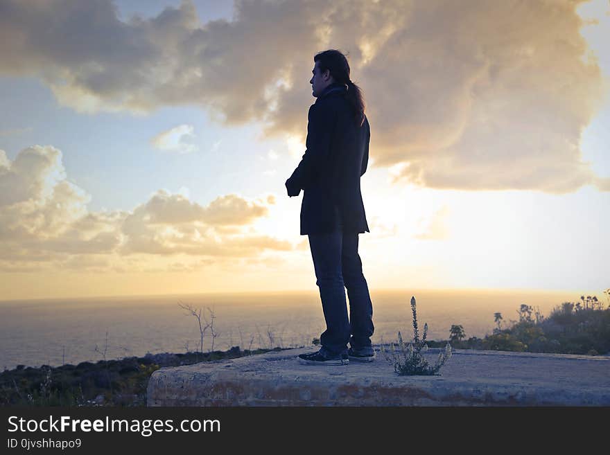 Man Wearing Black Coat Standing Near Sea during Golden Hour