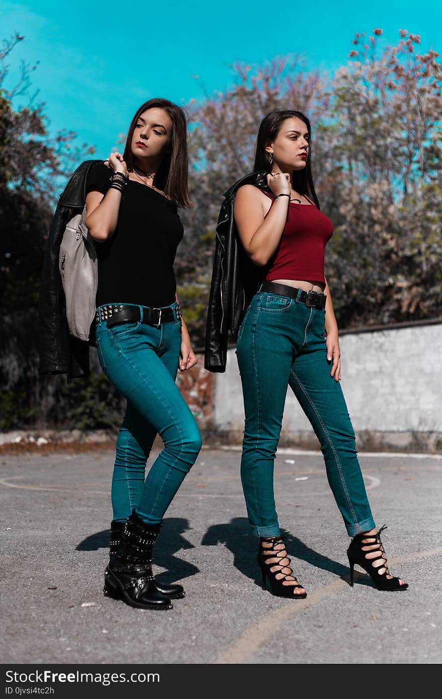 Woman in Black Cap-sleeved Shirt and Blue Denim Jeans Beside Woman in Red Spaghetti Strap Shirt Holding Black Leather Jacket at Daytime