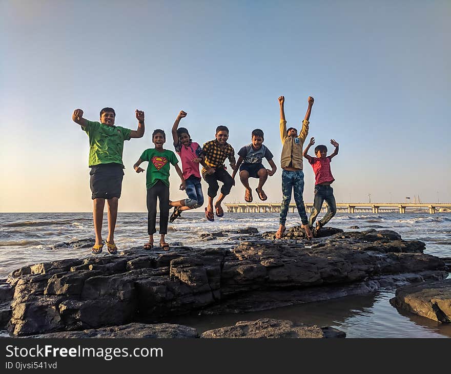 Boy Wearing Green Crew-neck Shirt Jumping from Black Stone on Seashore