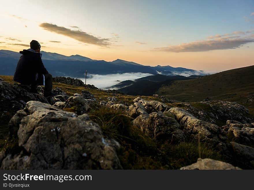 Person in Black Hoodie Sitting on Gray Stone