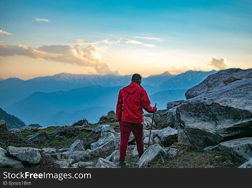 Man Wearing Red Hooded Jacket and Red Pants While Holding Black Metal Stick