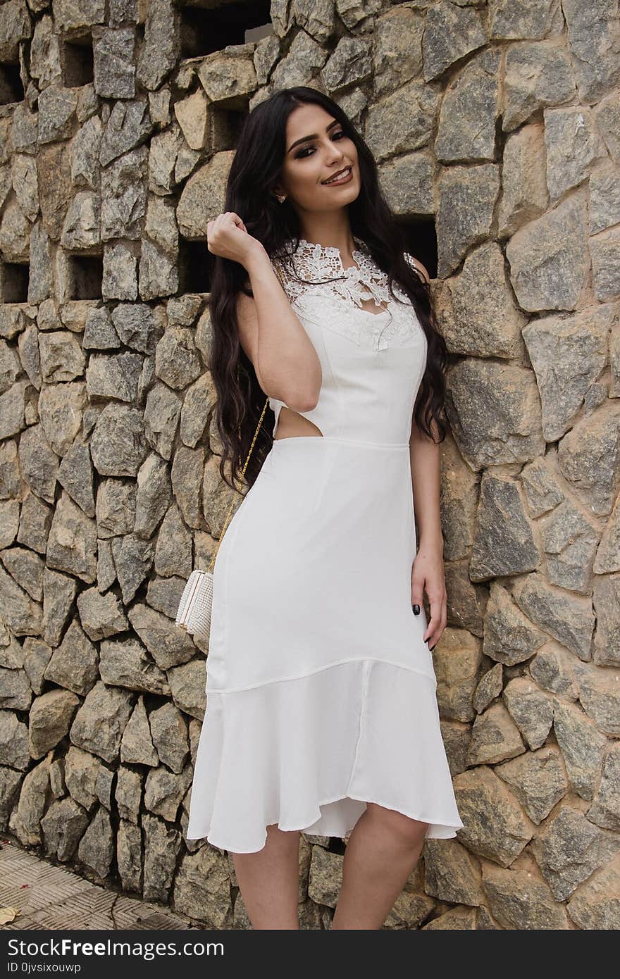 Woman in White Dress Leaning on Brick Wall Posing for Photo