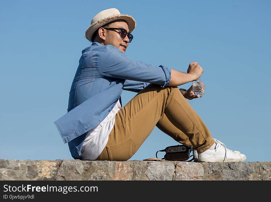 Asian tourist man open a bottle of water while sitting against