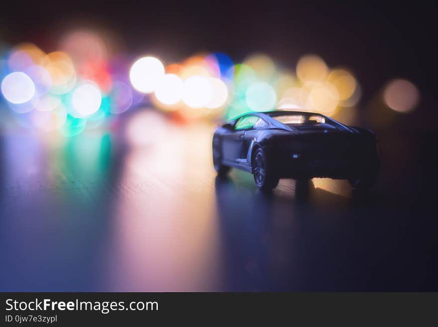 Small black car in dark night on the road and night multi-colored lights . the lights of the big city boheh , night traffic . car on night road. Small black car in dark night on the road and night multi-colored lights . the lights of the big city boheh , night traffic . car on night road