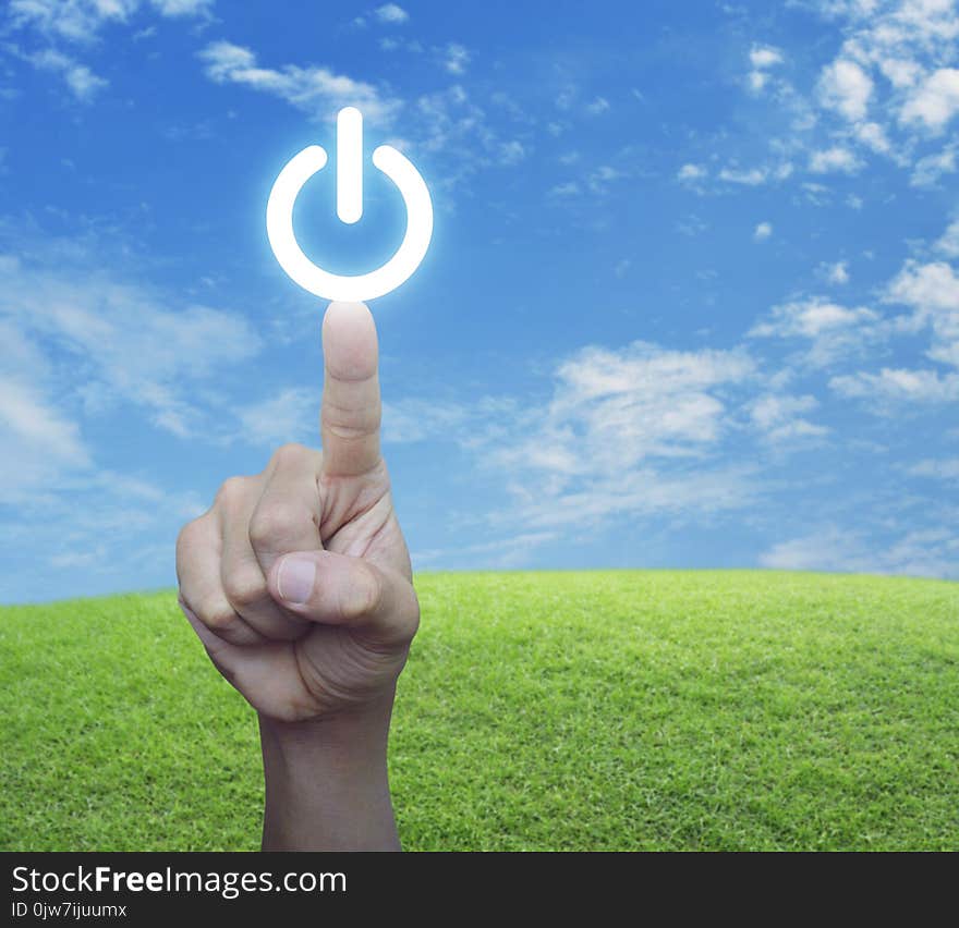 Hand pressing power button over green grass field with blue sky, Start up business concept