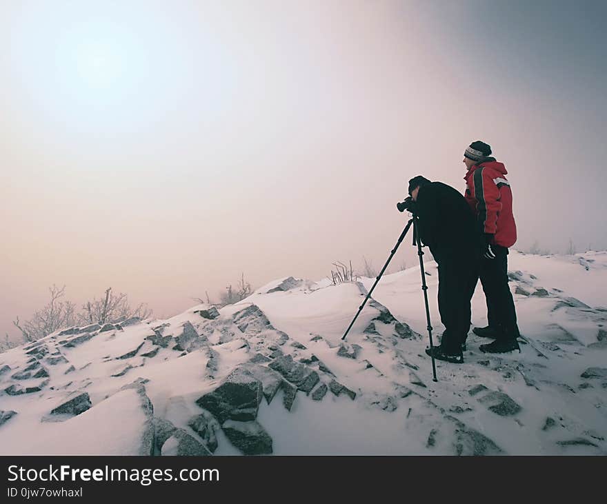 Hiker And Photo Enthusiast Stay On Snowy Peak At Tripod. Men On Cliff Speaking And Thinking.