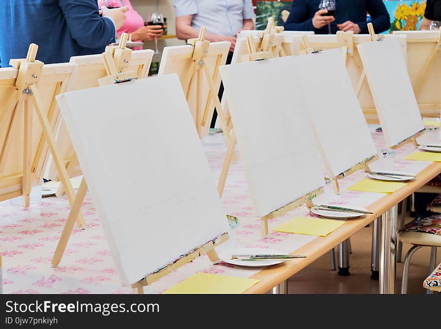 Canvases, brushes, palettes on the long wooden table ready for a masterclass in the art studio, people waiting to start drawing. Canvases, brushes, palettes on the long wooden table ready for a masterclass in the art studio, people waiting to start drawing