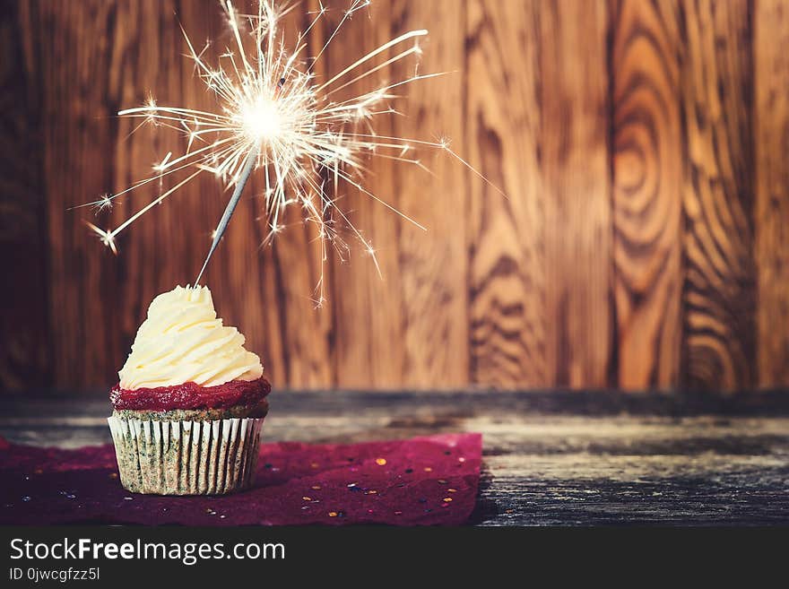 Cupcake with cream cheese, with sparkler on dark wooden background.