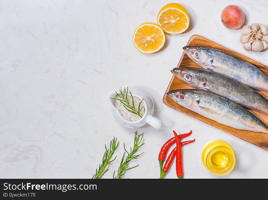 Fish dish cooking with various ingredients. Fresh raw fish decorated with lemon slices and herbs on wooden table.